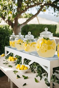 lemons and water in glass jars are on a table with greenery around them