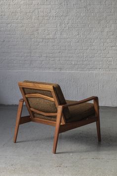 a wooden chair sitting in front of a white brick wall with a brown cushion on it