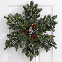 a wreath hanging on the front door of a house with red berries and pine cones