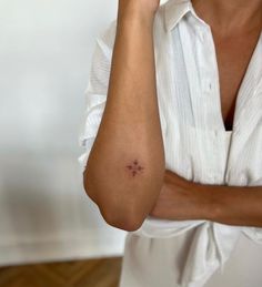 a woman wearing a white shirt and holding her arm up to her face with a small star tattoo on it