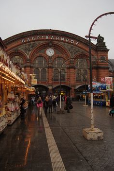 people are walking around in front of an old train station