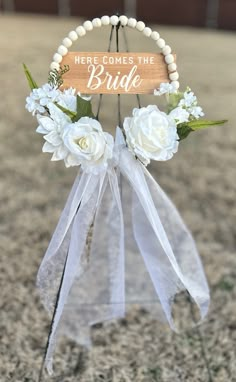 a sign that says here comes the bride hanging from a string with flowers on it