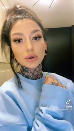 a woman with tattoos on her neck wearing a blue sweater and looking at the camera