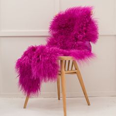 the chair is covered with purple fur and sits on a wooden frame in front of a white wall