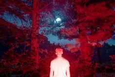 a man standing in the middle of a forest at night with red light coming from his head