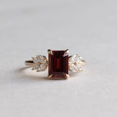 Metal: 14K Yellow Gold Stone: Emerald Cut Garnet  Stone Weight: 1.5 carat Stone Size: 5.75mm x 7.79mm Accent Stones: Natural Diamonds Accent Shapes: Marquise  Shank: 1.6mm Elegant Red Birthstone Ring With Vvs Clarity, Ruby Ring Designs, Red Engagement Ring, Wedding Rings Emerald Cut, Garnet Wedding Rings, Garnet And Diamond Ring, Red Garnet Ring, Red Sapphire, Cute Engagement Rings