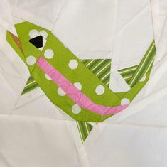 a green bird with white polka dots on it's body is sitting on a piece of fabric