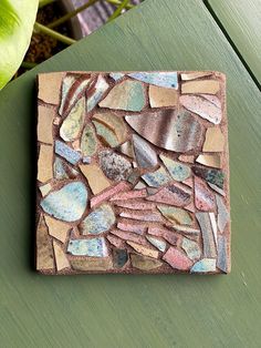 a green table topped with a small tile covered in lots of different colored rocks and pebbles