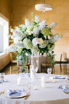 a vase filled with white flowers sitting on top of a table covered in blue and white plates