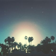 the sun shines brightly behind palm trees in front of a blue sky with stars