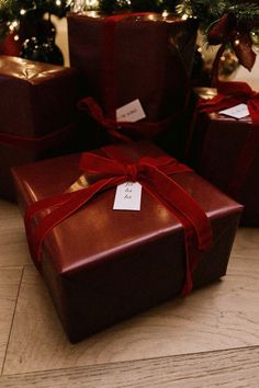 three presents wrapped in brown paper with red ribbon tied around them and sitting on the floor next to a christmas tree