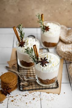 three desserts with cinnamon sticks and whipped cream in them on a cooling rack next to cookies