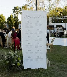 a white sign sitting on top of a lush green field next to a bunch of chairs