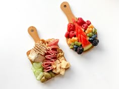 two wooden spoons filled with fruit and crackers next to each other on top of a white surface