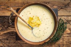 a wooden bowl filled with soup on top of a wooden table next to a spoon