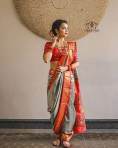 a woman in a red and grey sari is standing with her hand on her hip