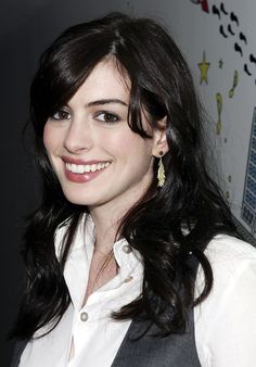 a woman with long dark hair smiling at the camera and wearing earrings on her ear