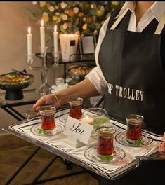 a woman holding a tray with tea cups and sauces on it in front of candles