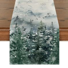 a table runner with trees and birds in the snow on it, against a wooden background