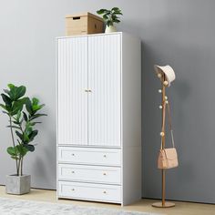 a white armoire next to a potted plant in a room with gray walls