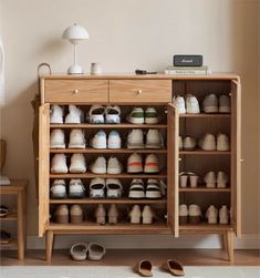 a wooden cabinet filled with lots of baby shoes next to a white wall and floor