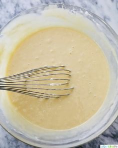 a mixing bowl filled with batter on top of a marble countertop next to a metal whisk