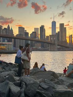 people are sitting on the rocks near the water and in front of a cityscape