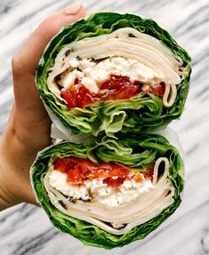 two wraps filled with lettuce and sauce on top of each other in front of a marble background