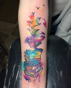 a colorful tattoo on the arm of a person with books and birds flying around it