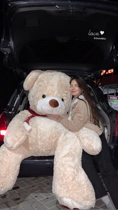 a woman sitting in the back of a car with a giant teddy bear next to her