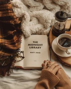 a person is reading a book on a bed next to a cup of coffee and a teddy bear