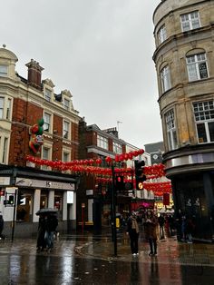 people are walking in the rain with umbrellas and red lanterns hanging over them on a city street