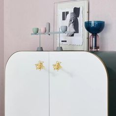 a white cabinet with two gold bee knobs on it's doors and a blue vase next to it