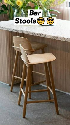 two wooden stools sitting next to a counter with flowers in vases on it