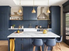 a large kitchen with blue cabinets and marble counter tops, along with bar stools