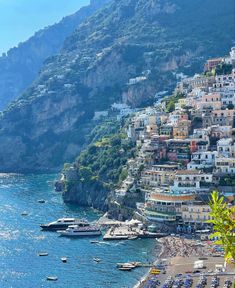 the beach is lined with boats and houses on the cliff side, along with mountains in the background