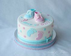 a white cake with blue and pink decorations on it's sides, topped with baby booties