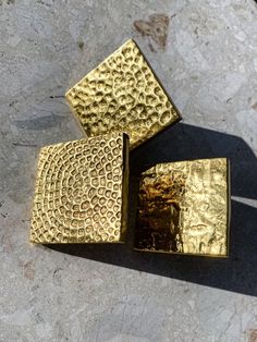 three pieces of gold sitting on top of a stone floor next to eachother