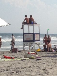 people are sitting on a lifeguard tower at the beach while others stand and sit in the water