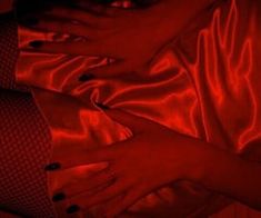 a woman laying on top of a bed covered in red sheets and pillows with her hands under her stomach