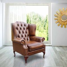 a brown leather chair sitting in front of a window next to a wall with a sun shaped mirror on it