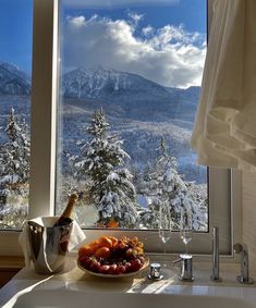 a bowl of fruit on a counter in front of a window with mountains and snow