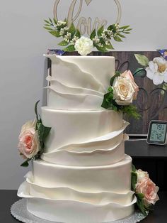 a three tiered wedding cake with roses and greenery on the side, next to a clock