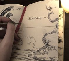 a hand holding a pen and writing on an open book with drawings in the pages