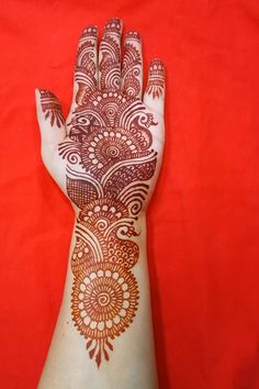 a hand with henna on it is shown against a red background and has intricate designs