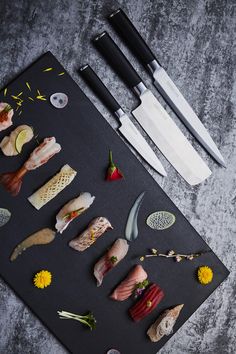 several different types of sushi on a cutting board next to knives and other kitchen utensils