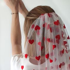 a woman wearing a veil with red hearts on it is holding her hands up to the ceiling