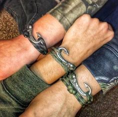 two men wearing bracelets and tattoos on their arms, both with rings around them