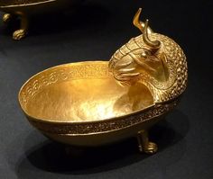 two gold bowls with bulls on them sitting next to each other in front of a black background