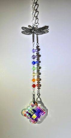 a multicolored dragonfly hanging from a metal chain on a white wall with the light reflecting off it's wing